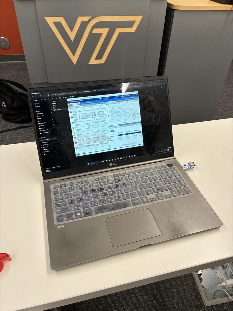 Laptop running EEG acquisition software with live channel traces, in front of a Virginia Tech podium.