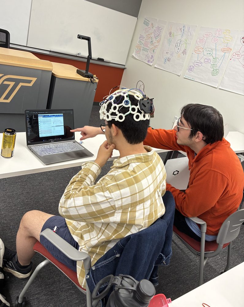 One member wearing the EEG cap while another points at the incoming signals on a laptop.